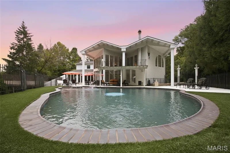 Expansive outdoor living area featuring a freeform swimming pool with a fountain, surrounded turf laid over the pool decking and a substantial patio space — 76 River Valley Drive, Chesterfield, MO 63017