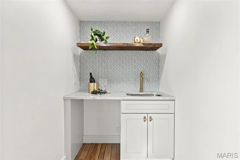 Wet Bar off family room with Brand new White cabinetry, gold-tone hardware, under mount sink with a brass-finish faucet, light-toned countertop, patterned tile backsplash, and a floating wood shelf — 621 Claymont Estates Drive, Chesterfield, MO 63017