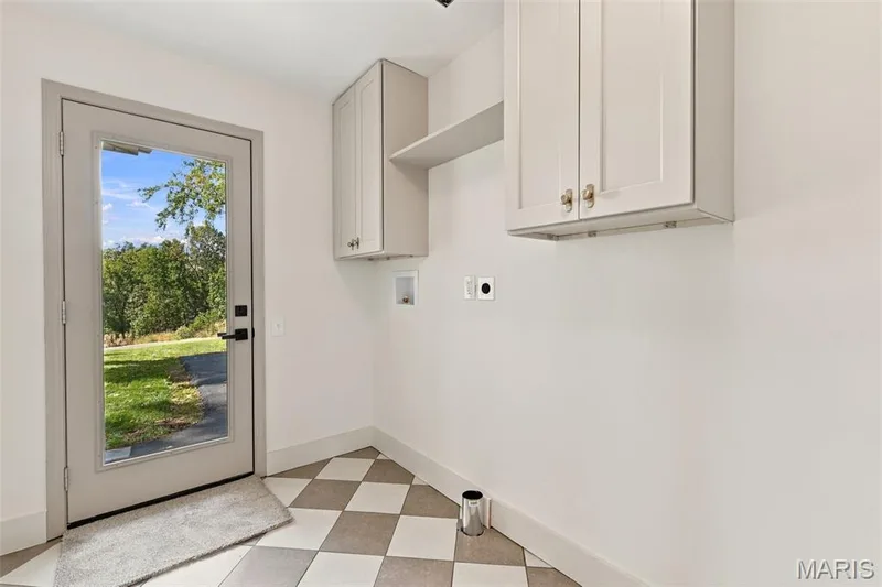 Main Floor Laundry Room off kitchen with checkered tile flooring, built-in upper cabinetry, and a door providing exterior access and door to access garage. — 621 Claymont Estates Drive, Chesterfield, MO 63017
