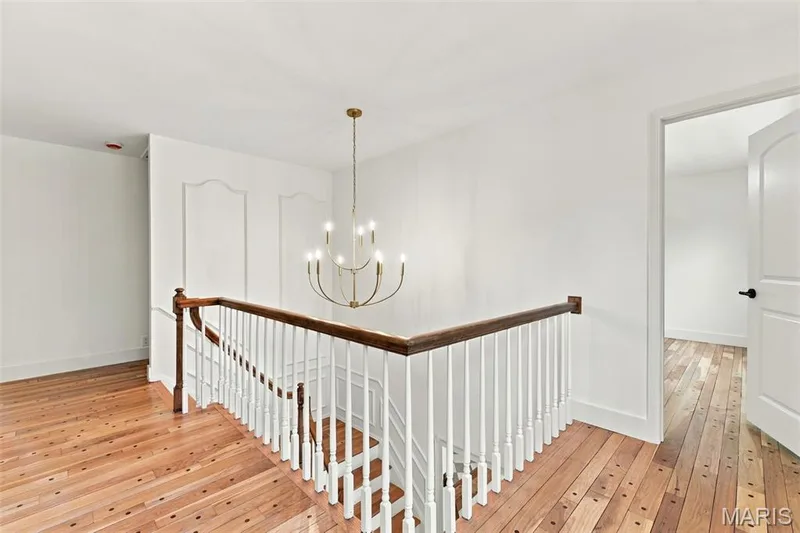 Upper level open stairway, Renewed Hardwood flooring throughout home, white painted walls, decorative wall molding, chandelier lighting, and a wood railing with white spindles — 621 Claymont Estates Drive, Chesterfield, MO 63017