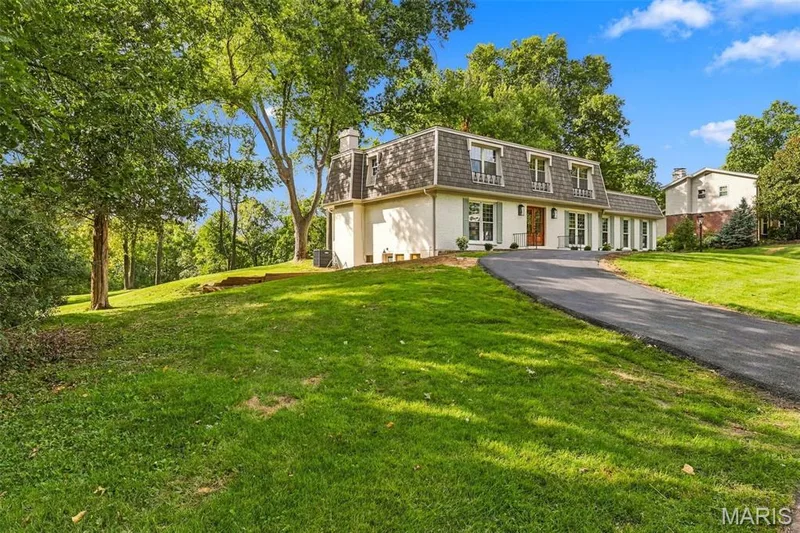 Dormer-style roofline, white exterior siding, light green window shutters, two wooden entry doors, and an asphalt driveway — 621 Claymont Estates Drive, Chesterfield, MO 63017