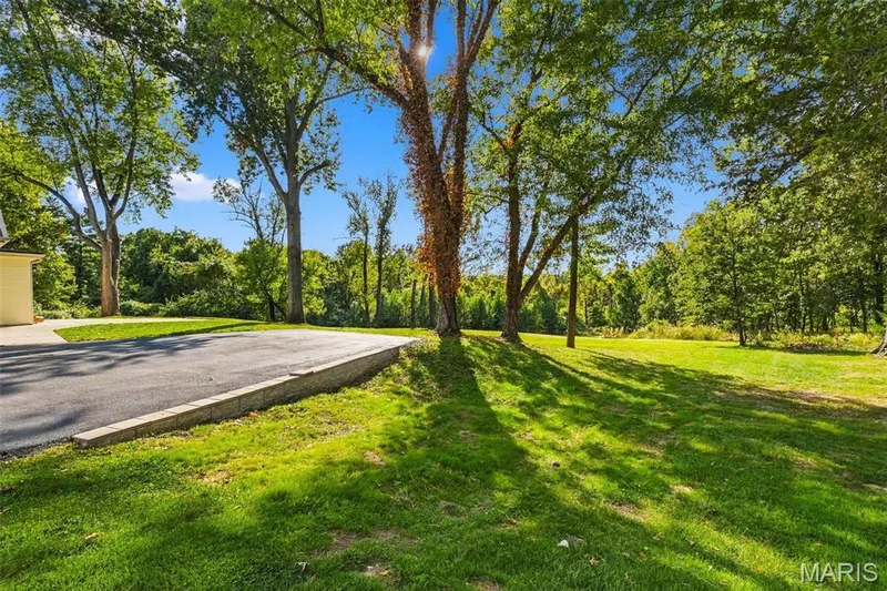 Rear garage w/ plenty of driveway space; Expansive green lawn with mature trees, bordered by a paved driveway and a low retaining wall — 621 Claymont Estates Drive, Chesterfield, MO 63017