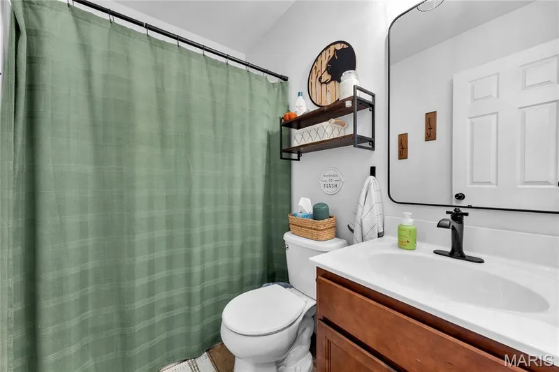 Bathroom featuring a wood-finish vanity with an integrated sink, matte black faucet, and rectangular framed mirror — 5507 Dressel Drive, Cottleville, MO 63304