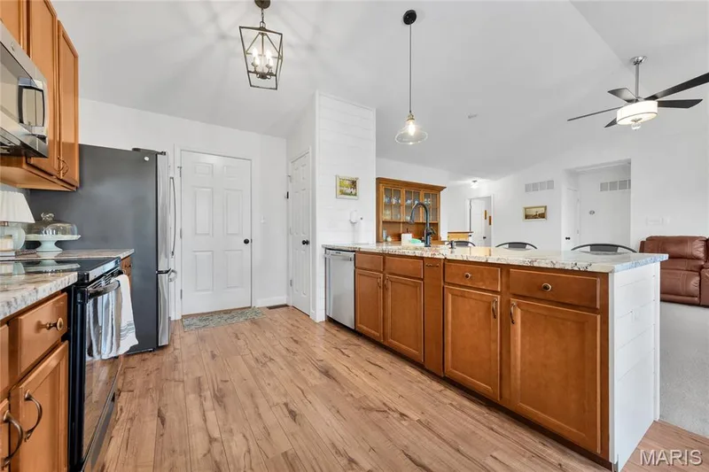 Kitchen featuring wood-finish flooring, wood cabinetry, stone countertops, and stainless steel appliances — 5507 Dressel Drive, Cottleville, MO 63304