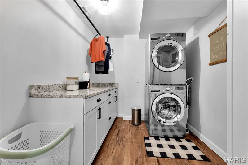Laundry area featuring wood-finish flooring, white cabinetry with black hardware, a light-toned countertop, and a ceiling-mounted light fixture — 5507 Dressel Drive, Cottleville, MO 63304