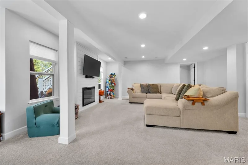 Recessed lighting, light-toned carpeting, window with privacy blind, electric fireplace with white shiplap surround, and built-in ceiling beams — 5507 Dressel Drive, Cottleville, MO 63304