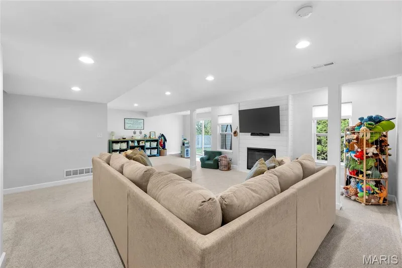 Carpeted living space with recessed lighting, a white brick fireplace, built-in shelving, and multiple windows — 5507 Dressel Drive, Cottleville, MO 63304