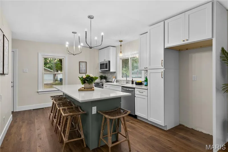Modern kitchen featuring a central island with countertop seating, white shaker cabinetry, stainless steel appliances, and wood-finish flooring — 924 N Benton Avenue, St Charles, MO 63301