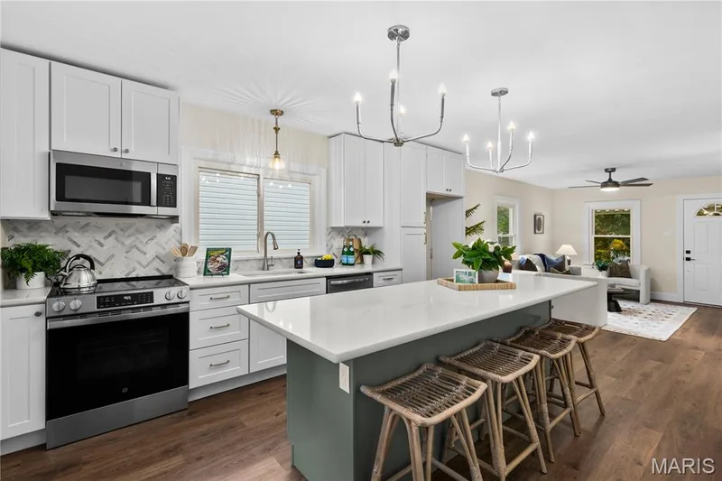 Modern kitchen featuring white shaker cabinetry, stainless steel appliances, a center island with seating, a herringbone-patterned tile backsplash, and wood-finish flooring — 924 N Benton Avenue, St Charles, MO 63301