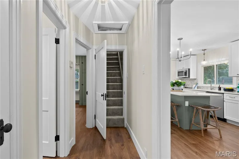 Wood-finish flooring, white paneled doors, carpeted stairs, and a kitchen featuring a central island with a light-colored countertop — 924 N Benton Avenue, St Charles, MO 63301