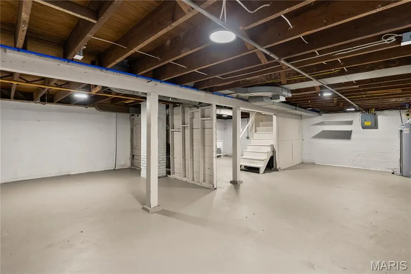 Expansive basement space featuring exposed wood joists, painted concrete flooring, and built-in shelving — 924 N Benton Avenue, St Charles, MO 63301
