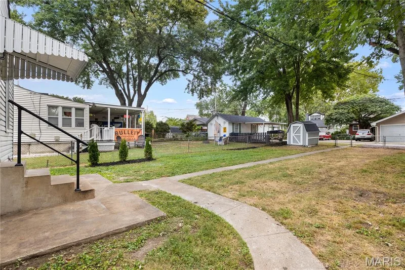 Concrete steps with black metal railing, white exterior siding, covered porch, concrete walkway, and a detached storage shed — 924 N Benton Avenue, St Charles, MO 63301