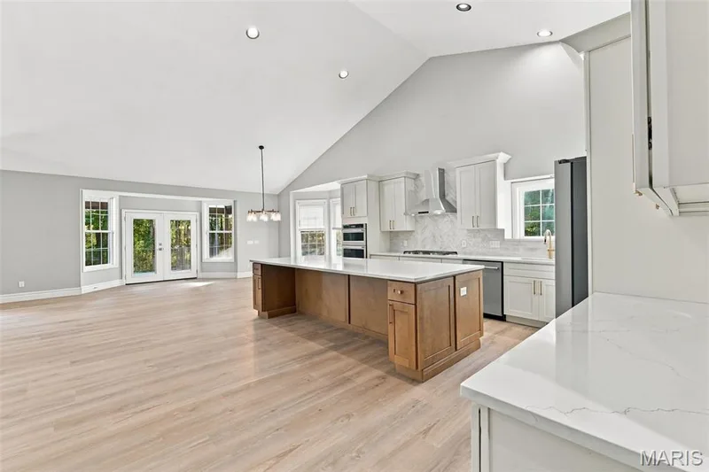 Vaulted ceiling, recessed lighting, luxury vinyl plank flooring, white shaker cabinetry, and a kitchen island with quartz countertops — 1580 Madre Drive, Foristell, MO 63348
