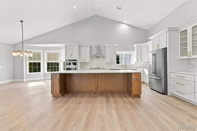 Vaulted ceiling, recessed lighting, luxury vinyl plank flooring, bay window, and a central island with white quartz countertops — 1580 Madre Drive, Foristell, MO 63348