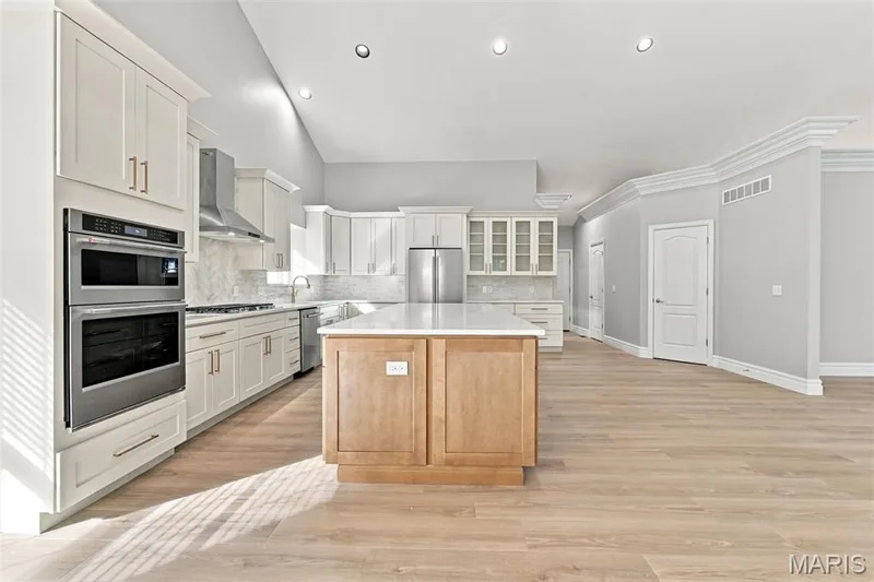 Modern kitchen featuring luxury vinyl plank flooring, white cabinetry, a built-in double oven, and a central island with a light-colored quartz countertop — 1580 Madre Drive, Foristell, MO 63348