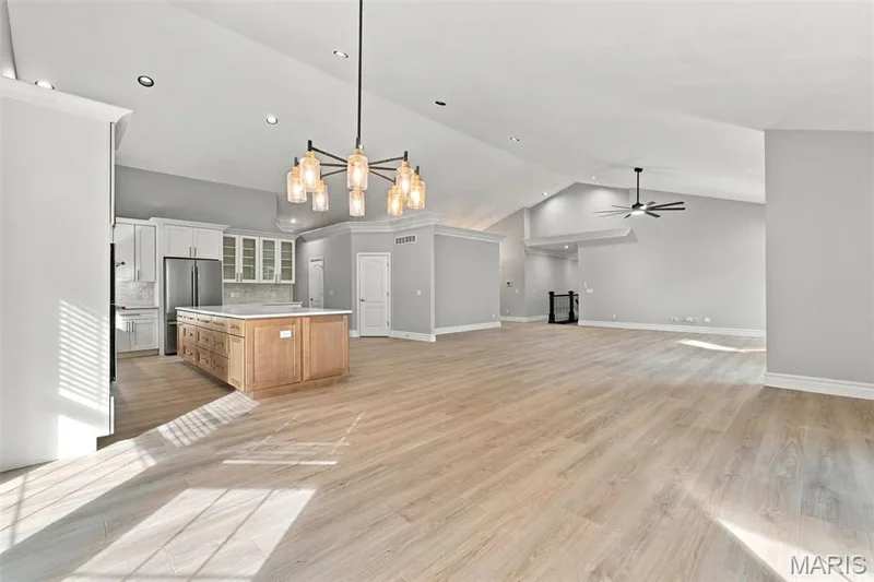 Open-concept room featuring luxury vinyl plank flooring, a kitchen island with storage, pendant lighting, and a vaulted ceiling with a ceiling fan — 1580 Madre Drive, Foristell, MO 63348