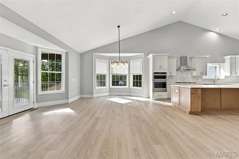 Open-concept living area featuring a vaulted ceiling, and a kitchen with an island, built-in microwave and oven, and stainless steel range hood — 1580 Madre Drive, Foristell, MO 63348