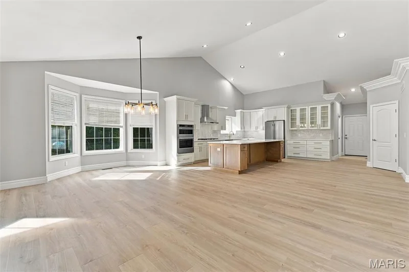 Vaulted ceiling with recessed lighting, luxury vinyl plank flooring, bay windows, kitchen island with counter seating, and built-in stainless steel appliances — 1580 Madre Drive, Foristell, MO 63348