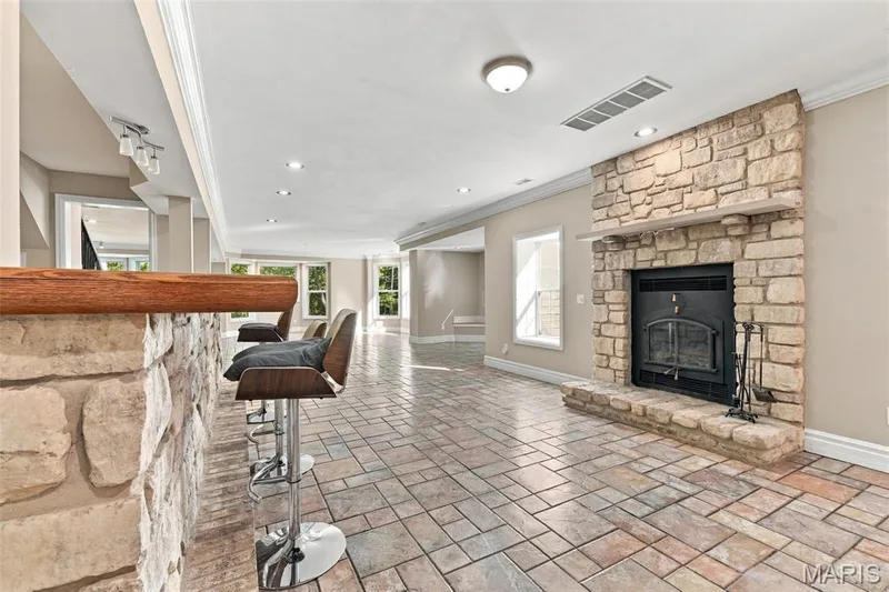 Stone-clad fireplace with hearth, built-in bar with wood top, recessed lighting, and patterned tile flooring — 1580 Madre Drive, Foristell, MO 63348