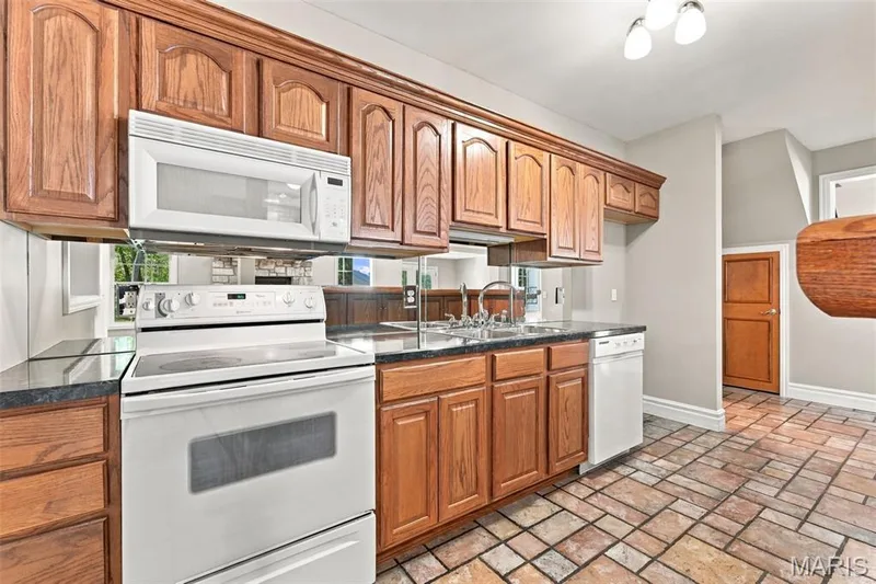 Wood cabinetry, dark countertops, a built-in microwave, a double basin sink, and tile flooring — 1580 Madre Drive, Foristell, MO 63348