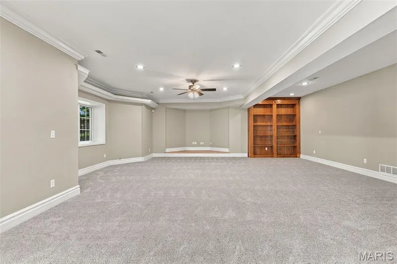 Expansive room with neutral carpet, recessed lighting, crown molding, a built-in wood bookcase, and a ceiling fan — 1580 Madre Drive, Foristell, MO 63348