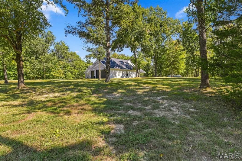 White siding exterior, dark roof, prominent garage doors, surrounding mature trees, and expansive grassy grounds — 1580 Madre Drive, Foristell, MO 63348