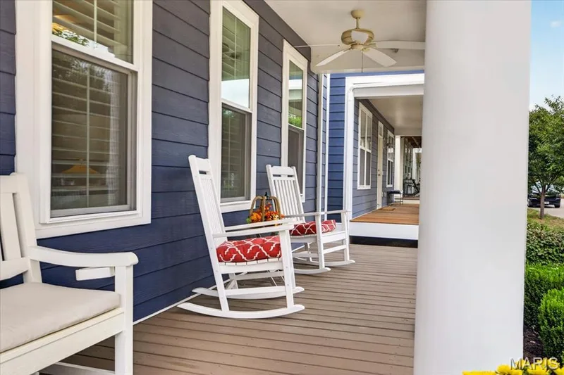 Expansive covered porch featuring wood-finish flooring, blue horizontal siding, white trim windows, and a ceiling fan — 3708 Broad Street, St Charles, MO 63301