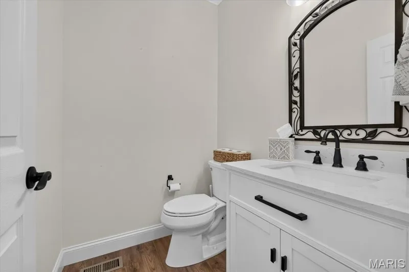 White vanity with integrated sink, black hardware, wood-finish flooring, and an ornate mirror — 3708 Broad Street, St Charles, MO 63301