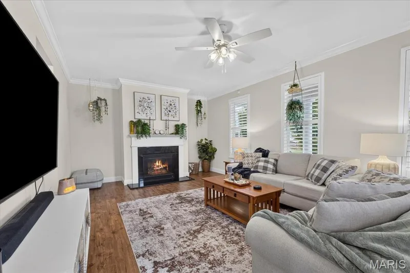 Living area with crown molding, wood-finish flooring, a fireplace with a white mantel, and ceiling fan — 3708 Broad Street, St Charles, MO 63301