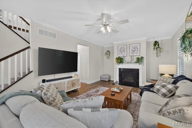 Living area featuring crown molding, a built-in fireplace with a white mantel, wood-finish flooring, and a ceiling fan — 3708 Broad Street, St Charles, MO 63301