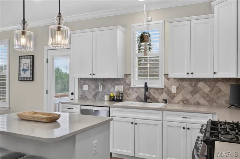 White cabinetry with black hardware, quartz countertops, herringbone pattern tile backsplash, and stainless steel appliances — 3708 Broad Street, St Charles, MO 63301