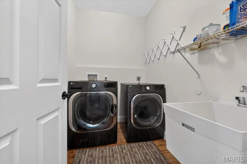 Equipped laundry area featuring a utility sink, wall-mounted shelving, and wood-finish flooring — 3708 Broad Street, St Charles, MO 63301