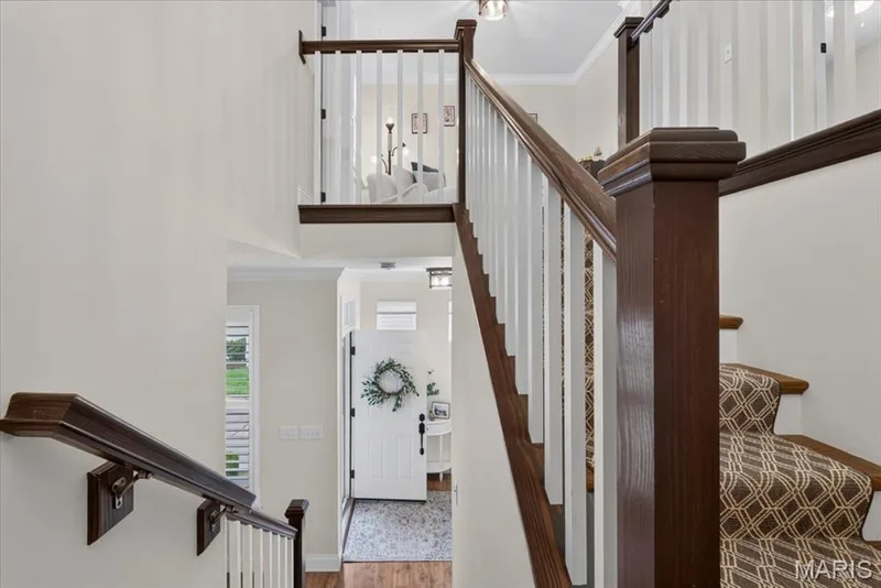 Two-story entryway featuring a wood-finish staircase with white balusters, a patterned stair runner, and a white paneled entry door — 3708 Broad Street, St Charles, MO 63301