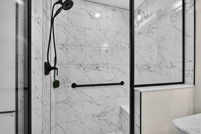 Shower enclosure featuring large format marbled wall tiles, a built-in bench, matte black fixtures, a grab bar, and a hexagonal tile floor — 3708 Broad Street, St Charles, MO 63301
