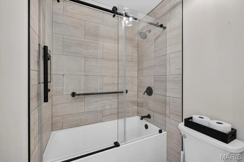 Tub and shower combination with full-height tile surround, clear glass sliding enclosure, and matte black fixtures — 3708 Broad Street, St Charles, MO 63301