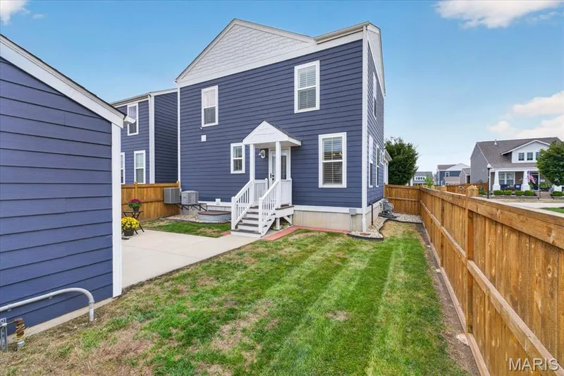 Fenced backyard featuring a manicured lawn, concrete patio, and a white-railed staircase leading to the rear entry — 3708 Broad Street, St Charles, MO 63301