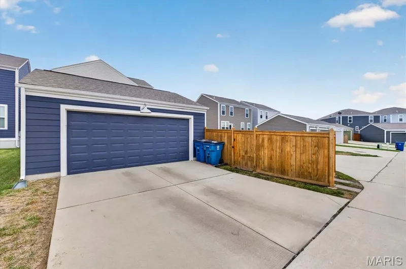 Attached garage with a panel-style door, concrete driveway, and wood privacy fencing — 3708 Broad Street, St Charles, MO 63301