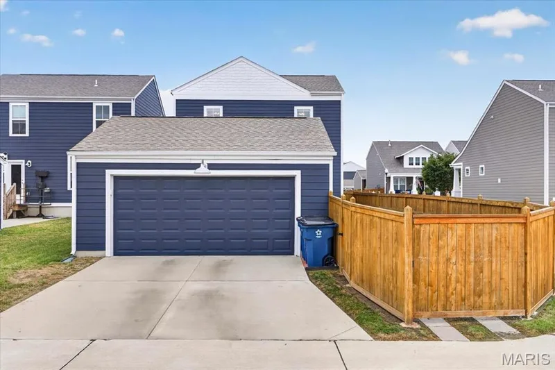 Attached two-car garage with a concrete driveway, blue siding, and a wooden privacy fence — 3708 Broad Street, St Charles, MO 63301
