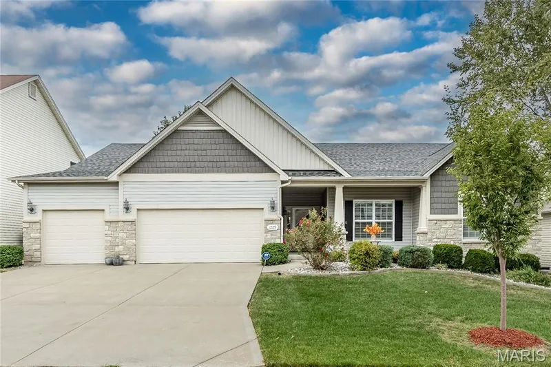 Gable roofline with shingle and siding accents, stone veneer exterior, covered front entry, two attached garages, and a concrete driveway — 1229 Cashmere Lane, St Peters, MO 63376