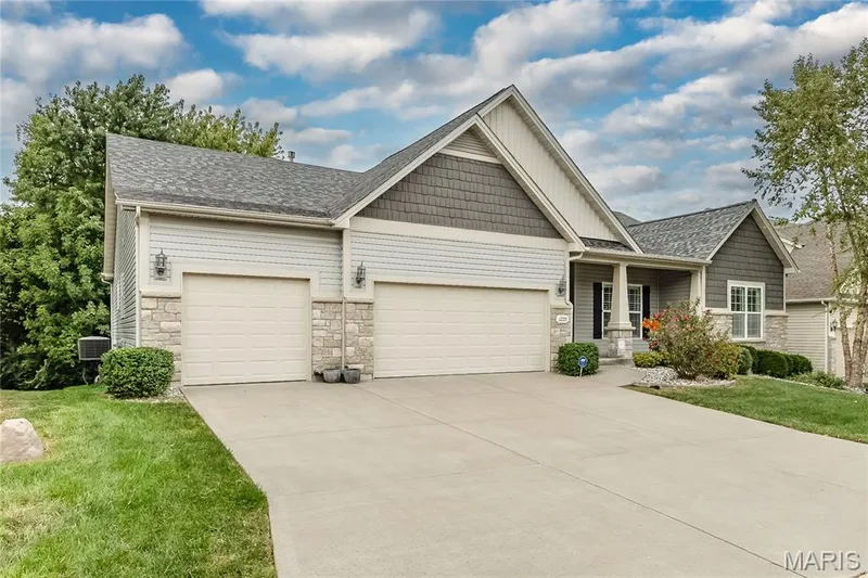 Contemporary exterior featuring light grey siding, stone accents, two garage doors, and a covered entry — 1229 Cashmere Lane, St Peters, MO 63376