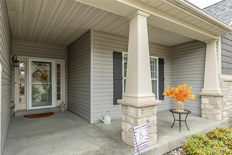 Covered front porch featuring stone-clad columns, horizontal siding, and a paneled front door with a storm door — 1229 Cashmere Lane, St Peters, MO 63376