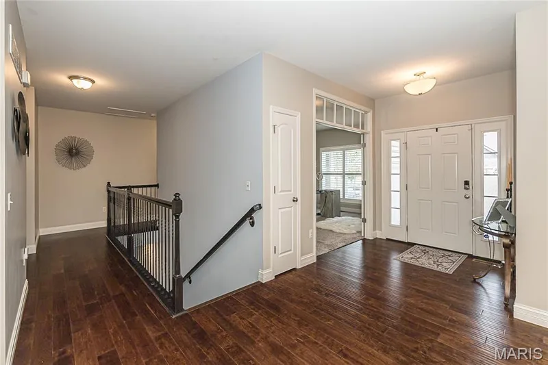 Hardwood-finish flooring throughout, white paneled entry door with sidelights, transom window above doorway, dark wood staircase banister, and overhead lighting fixtures — 1229 Cashmere Lane, St Peters, MO 63376