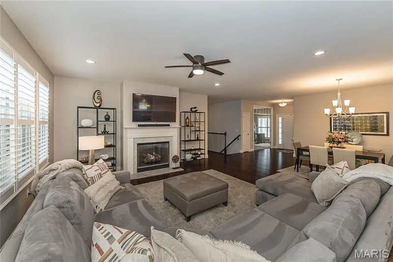 Living area featuring a fireplace with a white mantel, dark wood-finish flooring, recessed lighting, and white plantation shutters — 1229 Cashmere Lane, St Peters, MO 63376