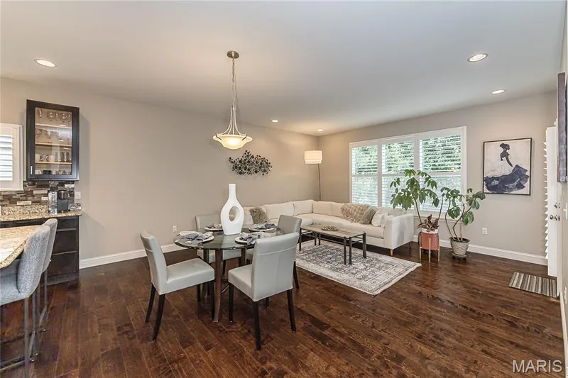 Hardwood-finish flooring throughout, recessed lighting, and a kitchen featuring dark wood cabinetry, a tiled backsplash, and stone countertops with an extended breakfast bar — 1229 Cashmere Lane, St Peters, MO 63376