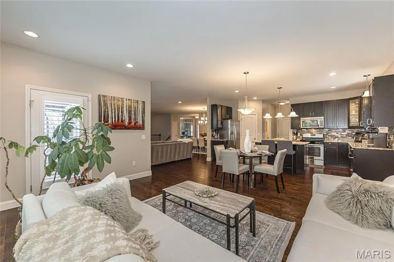 Open-concept living space featuring wood-finish flooring, recessed lighting, and a kitchen with dark cabinetry, stainless steel appliances, and granite countertops — 1229 Cashmere Lane, St Peters, MO 63376