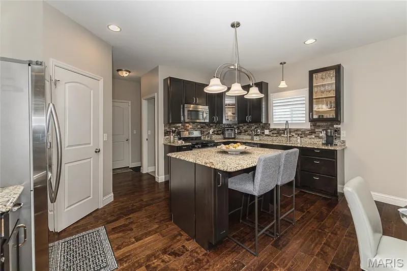 Kitchen featuring dark wood-finish cabinetry, granite countertops, stainless steel appliances, a center island with pendant lighting, and wood-finish flooring — 1229 Cashmere Lane, St Peters, MO 63376
