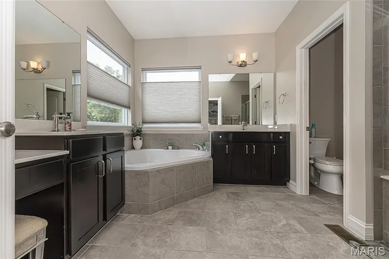 Dual dark wood vanities with integrated sinks, a corner soaking tub, and tile flooring — 1229 Cashmere Lane, St Peters, MO 63376