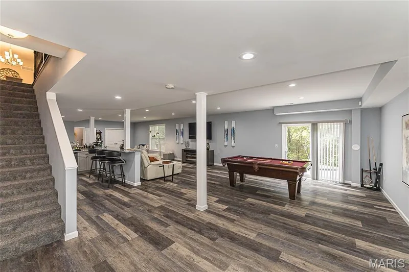 Expansive open-concept recreation space with wood-finish flooring, recessed lighting, and a built-in bar area with seating — 1229 Cashmere Lane, St Peters, MO 63376