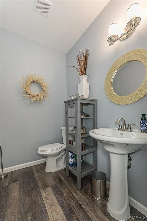 Wood-finish flooring, pedestal sink with brushed nickel faucet, wall-mounted light fixture, and a toilet — 1229 Cashmere Lane, St Peters, MO 63376