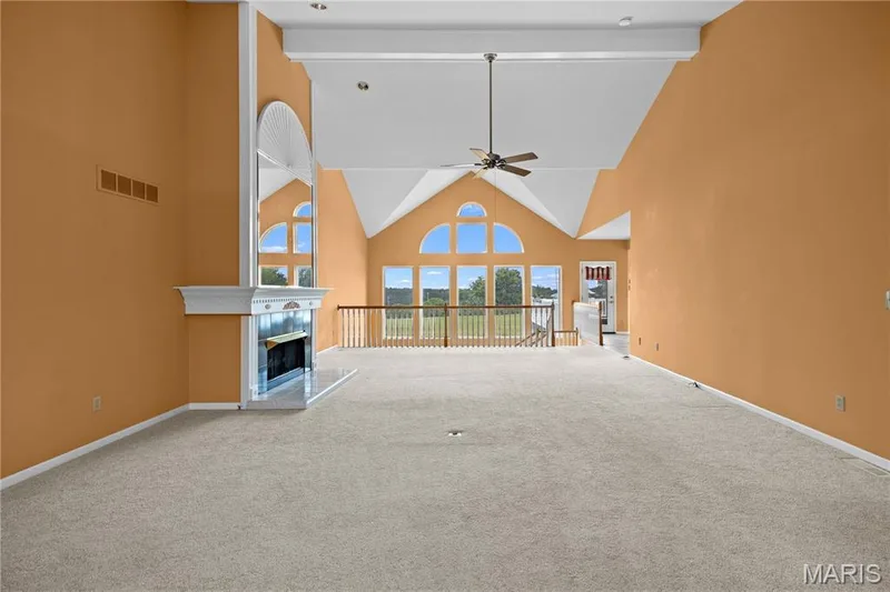 Vaulted ceiling with exposed beam, arched windows, built-in fireplace, ceiling fan, and carpeted flooring — 104 Wolf Trail Court, Defiance, MO 63341